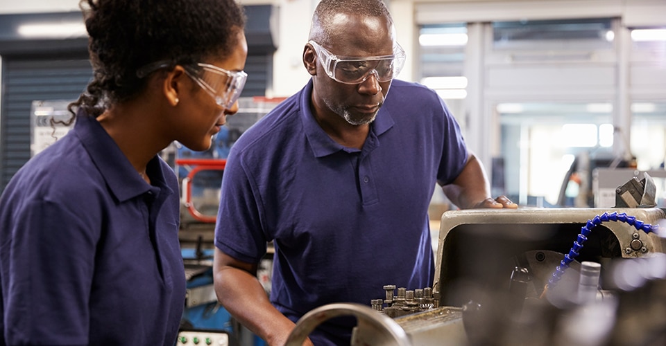 One employee watches another do machine work